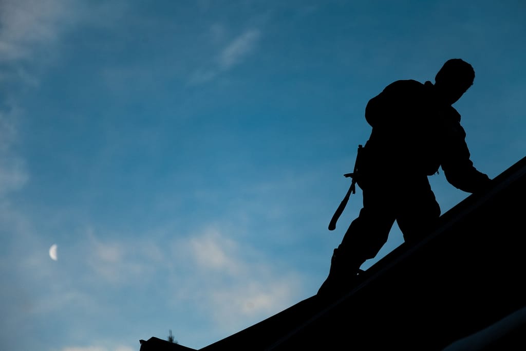 Contractor in Silhouette working on a Roof Top with blue Sky in Background - roofing contractors - Home Crafters